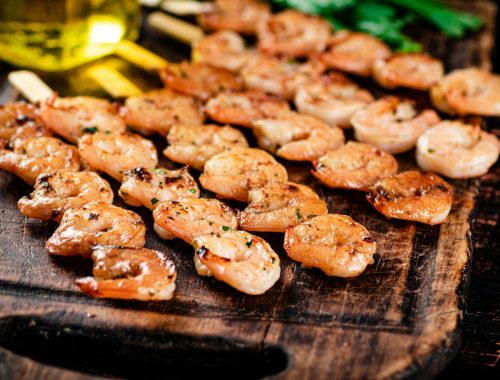 Grilled shrimp on skewers with parsley on a cutting board.