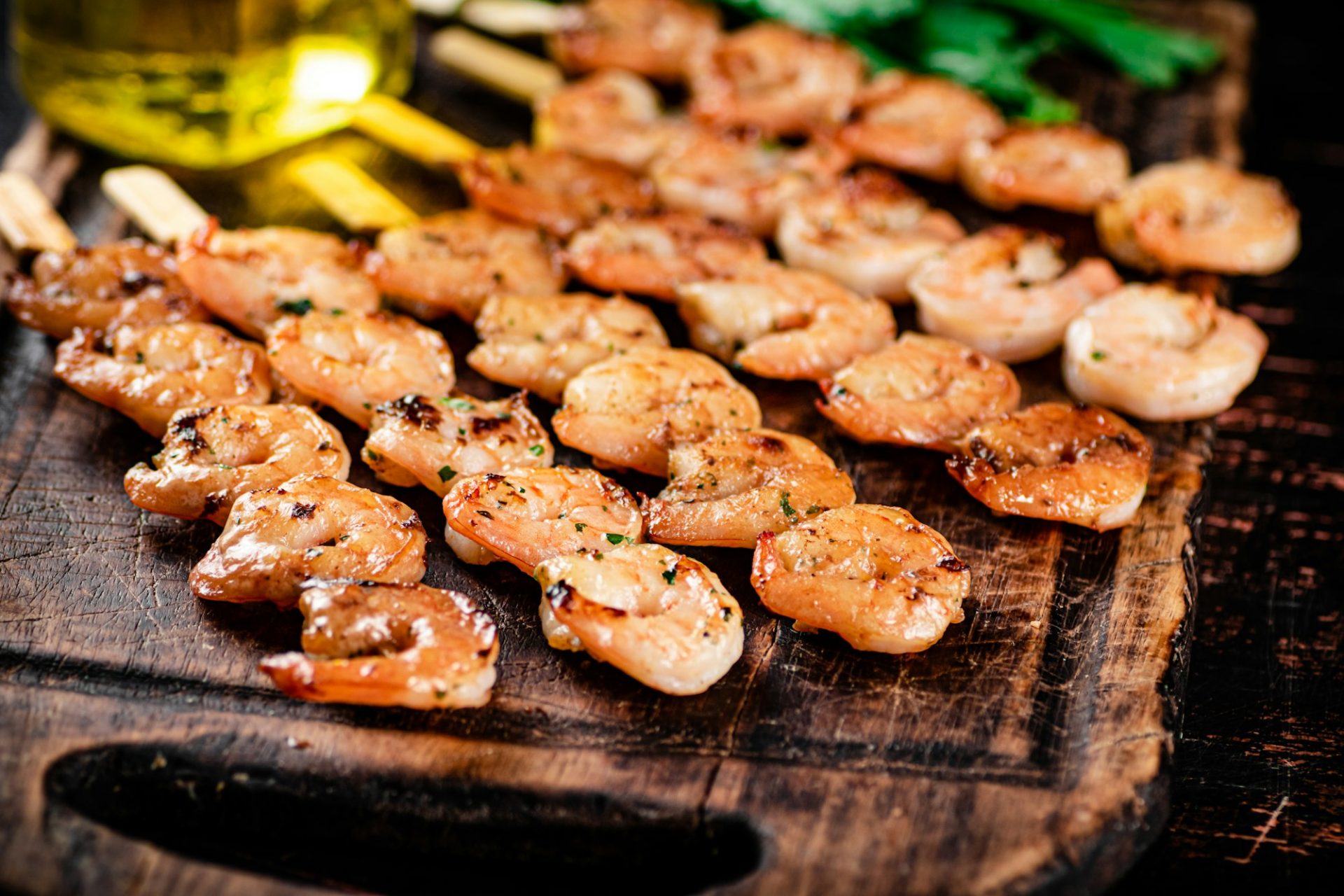 Grilled shrimp on skewers with parsley on a cutting board.